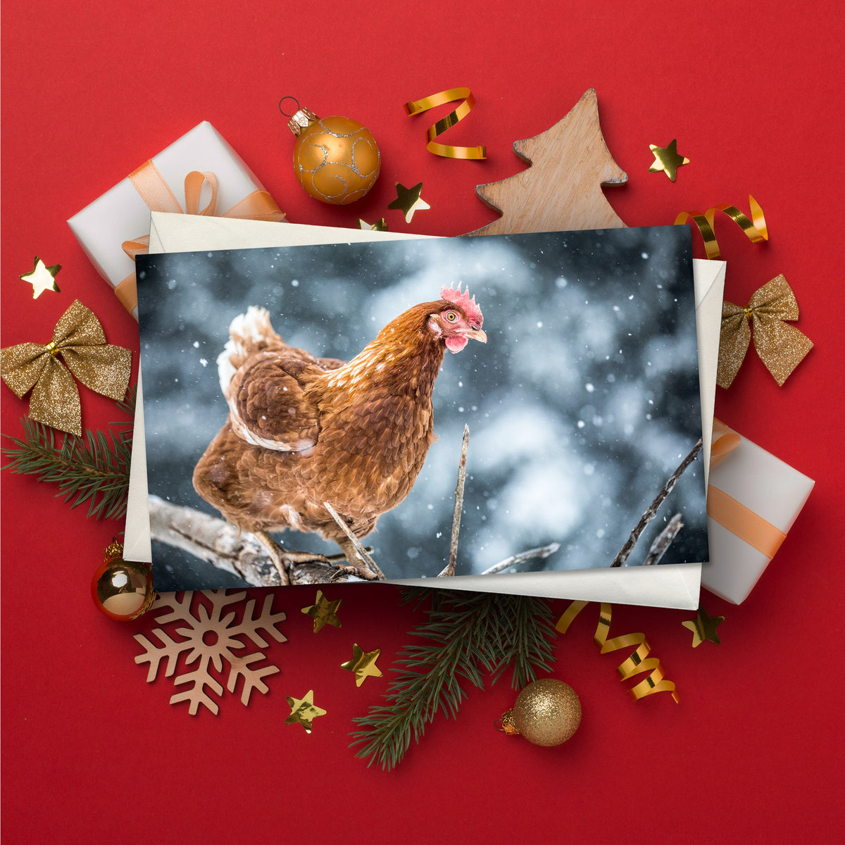 Christmas card showing a brown hen perched on a branch during falling snow, surrounded by wrapped gifts, gold baubles, stars and festive decorations on a red background.